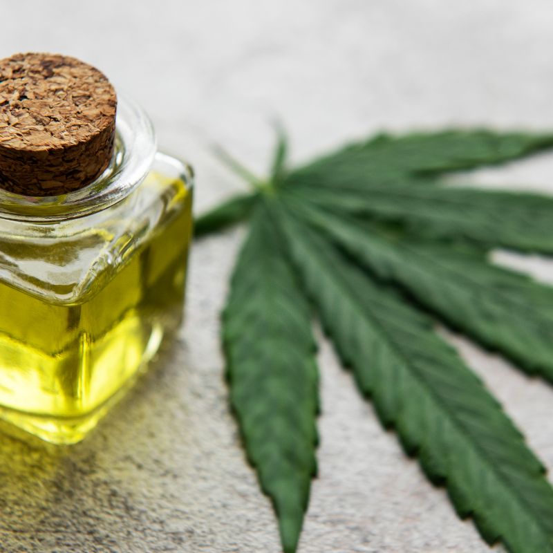 An image of a cannabis leaf next to a glass jar of oil.