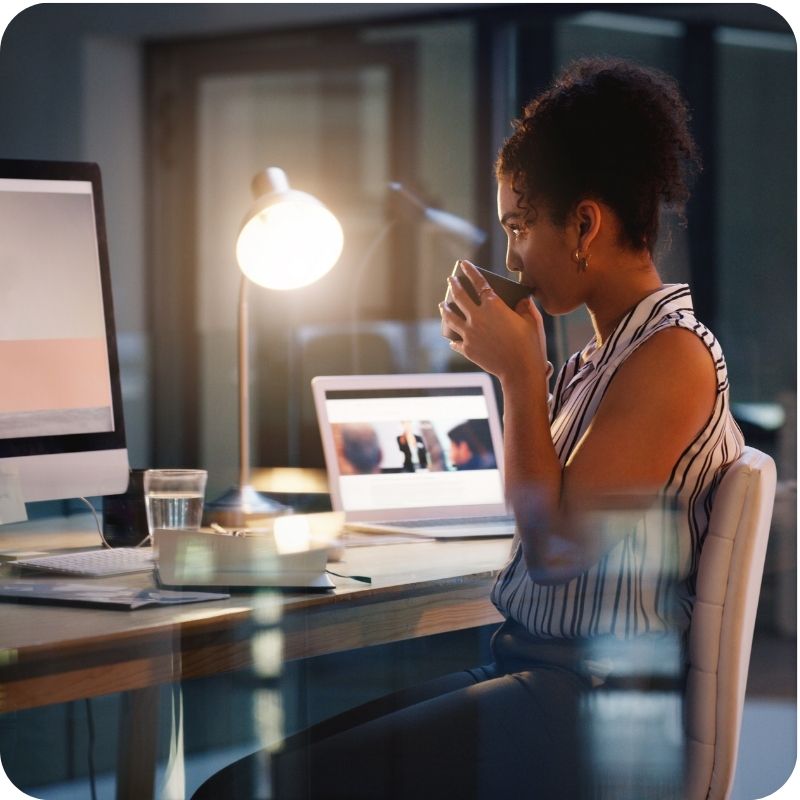 Image of a person drinking coffee at their desk while working on a laptop.