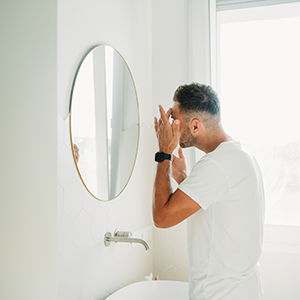 A millennial man is using a face cream in the bathroom. Man's care beauty routine.