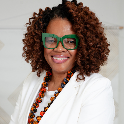 Woman with curly hair and green reading glasses smiling 