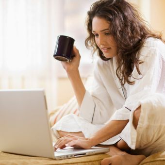 Woman sitting cross legged looking at a laptop screen holding a mug