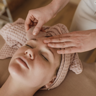 Woman with beige towel wrapped around her head receiving a facial from an esthetician