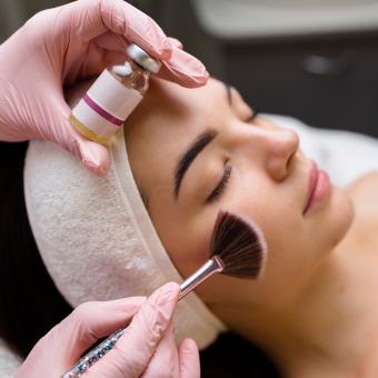 Esthetician wearing pink latex gloves performs a chemical peel on a client