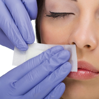 An esthetician applies a wax strip on their client's lip during a lip and chin waxing service.