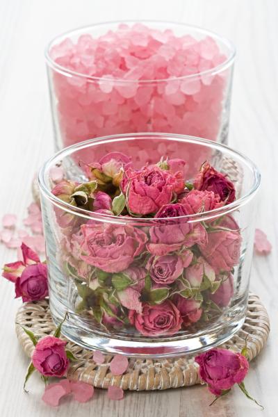 Dried roses for a DIY rose sugar scrub and pink crystals are displayed in glass jars.