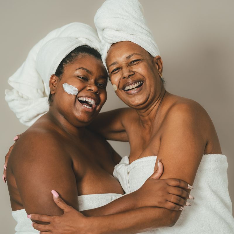 Image of two people in bath towels hugging and smiling. 