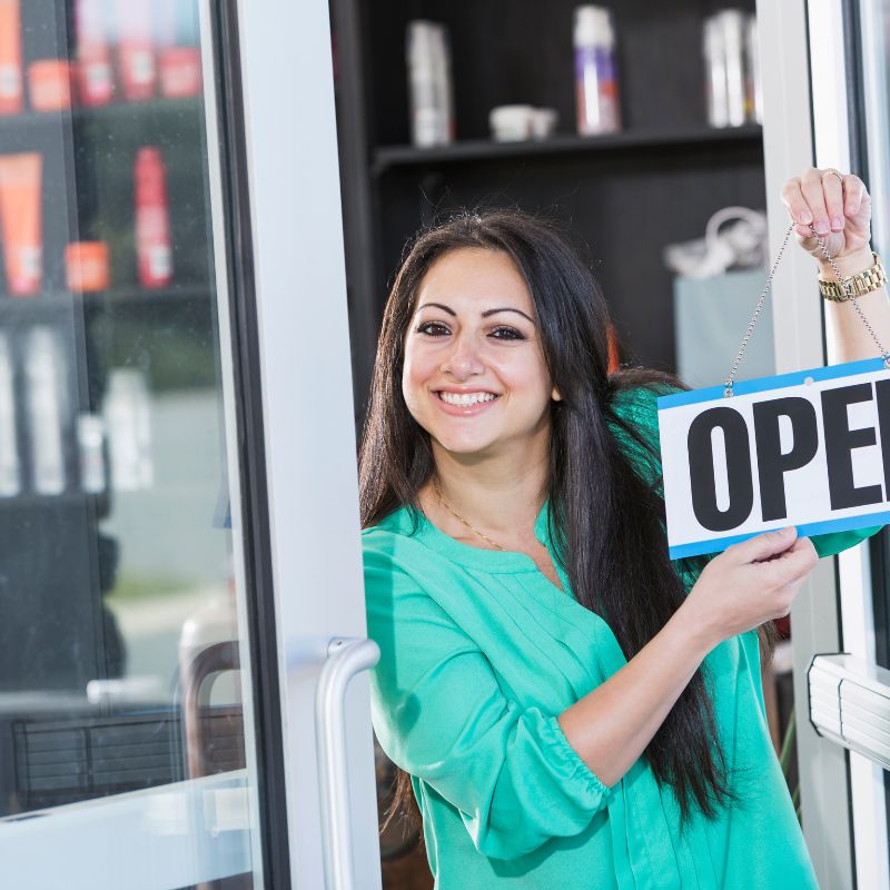 A person standing in a doorway holding an open sign.