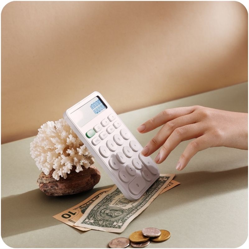 Image of a person using a calculator with dollar bills and change on the table.