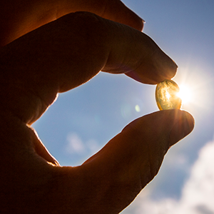 Yellow soft shell D-vitamin capsule against sun and blue sky on sunny day. 