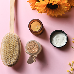 Dry Brush Placed With Scented Candles And Organic Moisturizer On Pink Background