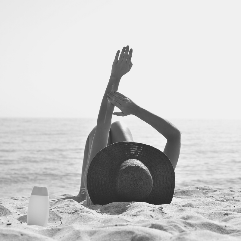 woman sunbathing at the bean and applying SPF to her arm