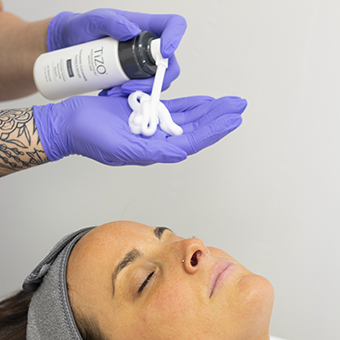 Esthetician cleansing client's skin before chemical peel