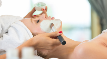 Esthetician applies green mask to client's face