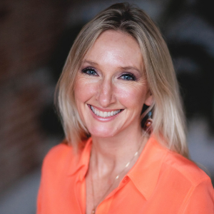 Blonde woman in an orange blouse smiling at camera 